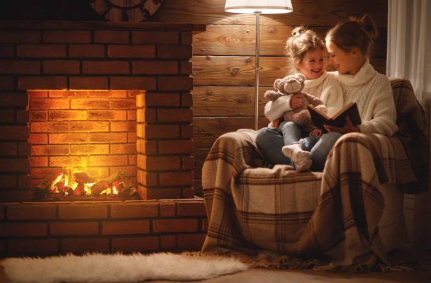 happy family mother and child daughter read book on winter evening near energy efficient fireplace